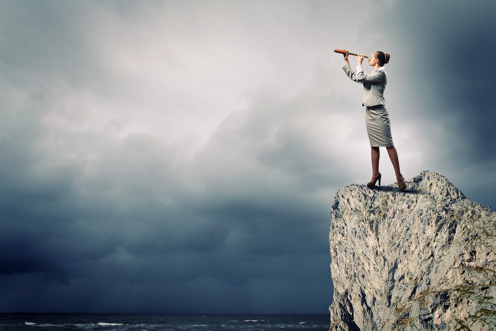 Image of businesswoman looking in telescope standing atop of rock